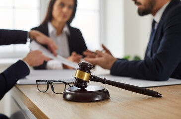 Close up of judge's gavel and glasses on table, with lawyer meeting with group of angry,...