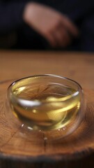 A delicate glass bowl with shimmering golden tea rests elegantly on a wooden surface. Media