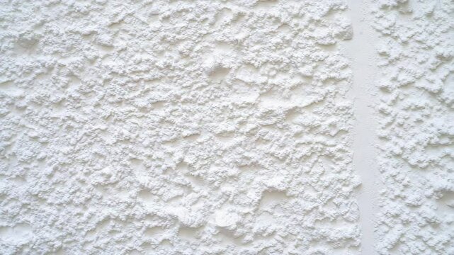 Close-up of a white textured wall with rough, bumpy stucco finish, providing a clean and abstract architectural surface.