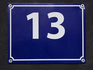 number 13 is stenciled in blue frame on black concrete wall, copy space. House number Thirteen on...