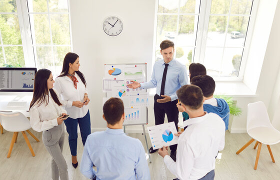 Business coach speaker in office gives presentation, male speaker presenter consulting, training persuading employees client group, mentor leader explains company graph strategy at team meeting 