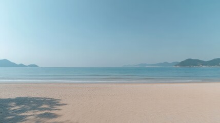 Tranquil beach scene.  Soft, blurred view of a sandy beach meeting a calm ocean under a clear sky.  Gentle waves, distant hills
