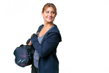 Middle-aged sport woman with sport bag over isolated background with arms crossed and happy
