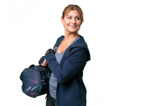 Middle-aged sport woman with sport bag over isolated background with arms crossed and happy