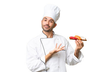 Young caucasian chef holding a sushi over isolated background extending hands to the side for inviting to come