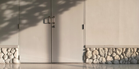 Sunlight and shadow of tree on the door and white wall with artificial stone decoration on low section of wall, home interior modern architecture background in minimal style
