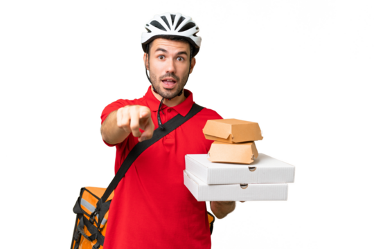 Young handsome caucasian man with thermal backpack and holding takeaway food over isolated background surprised and pointing front