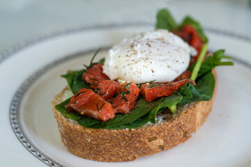 delicious breakfast poached egg on a slice of ciabatta with spinach and pieces of red salted fish