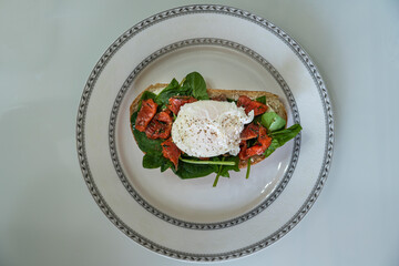 delicious breakfast poached egg on a slice of ciabatta with spinach and pieces of red salted fish