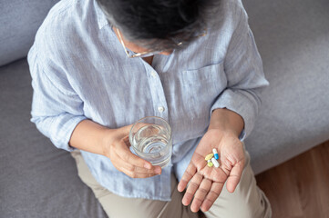 Top view close up hand of an elderly Asian woman is pouring vitamins from a bottle to take for...