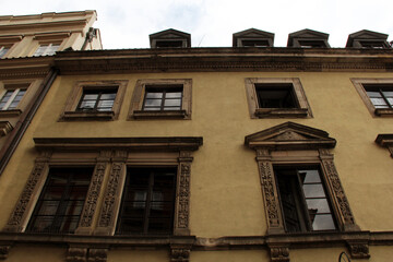 Obraz premium Ornate facade of an old European building with richly carved stone window frames, symmetrical architecture, dormer windows, and pale yellow plaster walls — traditional city design in heritage district
