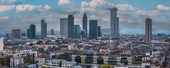 Fototapeta premium Aerial view of Frankfurt, Germany, highlighting the Messeturm, Tower 185, and Hauptbahnhof. Modern and traditional buildings with hills in the distance.