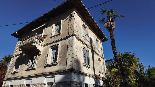 Looking up view of an old romantic villa in Lovran, Istria - Croatia. Beautiful mediterranean building and some palm trees against the blue sky on a sunny day. Slow motion panning video.