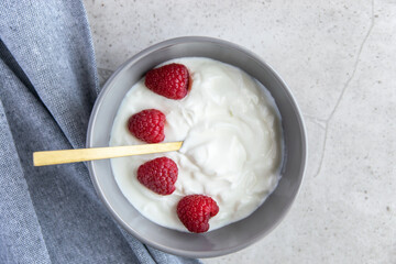 Gray bowl and natural yogurt with berries on the stone marble table.
