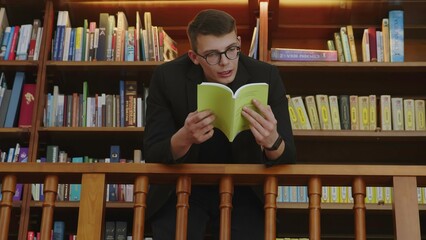 A young man deeply engaged in reading a book within the warm, inviting ambiance of a cozy library. Media