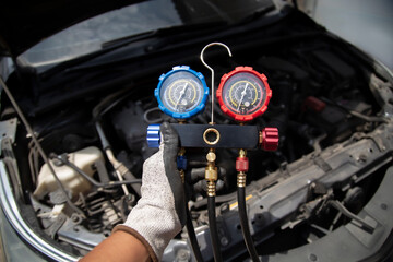 Auto mechanic's hand uses a meter to check for problems with the car's air conditioning system and...