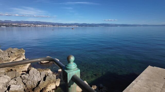 Green railings of the Lungomare Coastal Promenade near Lovran, Croatia. Rocky coastline of the Adriatic Sea with Rijeka in the background. The famous seaside promenade is more then 100 years old.