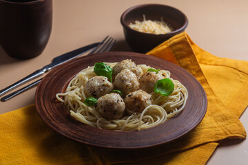 Spaghetti with meatballs in creamy sauce in a brown plate on a yellow background