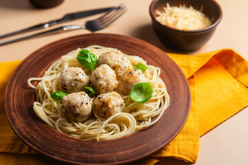 Spaghetti with meatballs in creamy sauce in a brown plate on a yellow background