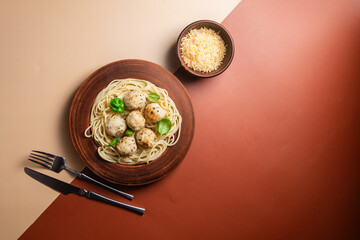 Spaghetti with meatballs in creamy sauce in a brown plate on a yellow background