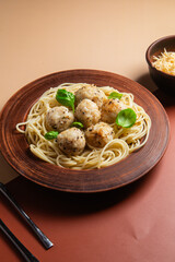 Spaghetti with meatballs in creamy sauce in a brown plate on a yellow background