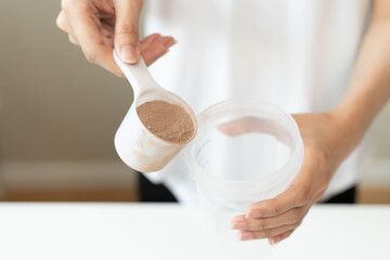 Young sporty woman pouring protein powder into a cup to make replacement food meal after workout