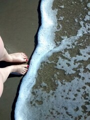 pés femininos com unhas pintada de vermelho na beira do mar com onda se aproximando 