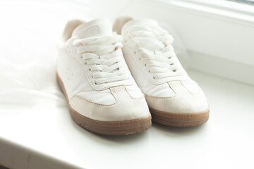 A pair of crisp white sneakers sit near a window, casting a bright and clean aesthetic. These trainers offer style and comfort.