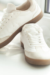 A pair of off-white, retro-style sneakers with brown soles sit atop a softly lit, white surface, showcasing simple and clean design.