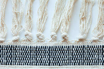Close-up of woven textile with knotted fringe, showcasing texture and detail in its construction.  Intricate weave pattern.