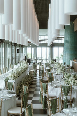 Wedding. Banquet. The chairs and round table for guests, served with cutlery, flowers and crockery and covered with a tablecloth,  green and white theme.