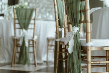 Wedding. Banquet. The chairs and round table for guests, served with cutlery, flowers and crockery and covered with a tablecloth,  green and white theme.