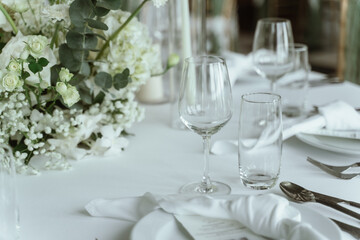 Wedding. Banquet. The chairs and round table for guests, served with cutlery, flowers and crockery and covered with a tablecloth,  green and white theme.