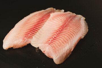 Fresh tilapia fillet on black background, top view.