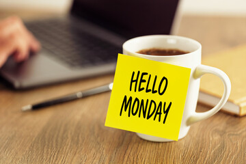 Coffee cup with hello monday sticky note on wooden desk with laptop and pen symbolizing workplace...
