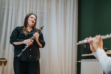 A musician demonstrates clarinet techniques to a student with a flute in a class setting.