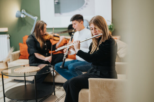 Musicians play flute, violin, and clarinet in a stylish living room. The ambiance is cozy, featuring modern furniture and a creative atmosphere, highlighting the joy of music and companionship.
