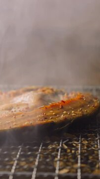 Smoking delicious fresh ide fish steak with rising up hot steam on metal grid lying on pile of wooden chips and charcoals closeup slow motion