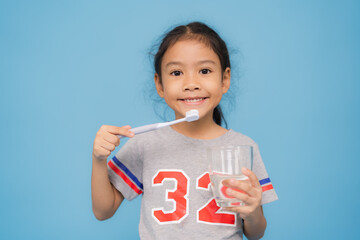 Happy little girl brushing teeth and holding glass of water