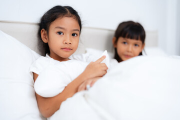 Two happy little asian sisters lying and playing in bed