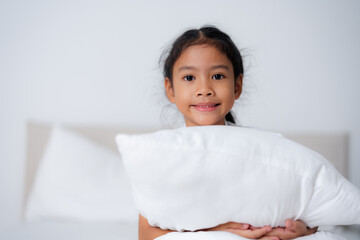 Happy girl hugging pillows on bed in bedroom