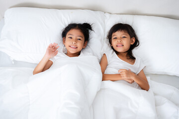 Two cute asian children waking up and stretching in bed