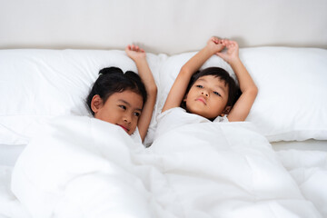 Two cute asian children waking up and stretching in bed