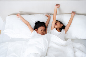 Two cute asian children waking up and stretching in bed