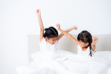 Two cute asian children waking up and stretching in bed