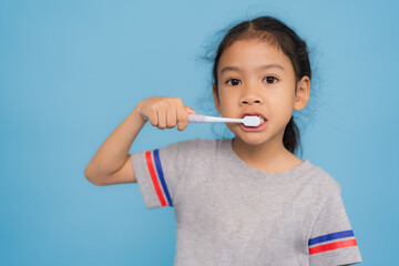Young girl brushing teeth with toothbrush on blue background