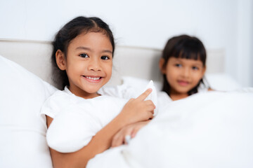 Two happy little asian sisters lying and playing in bed