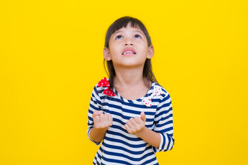 Little girl looking up with hope and clenched fists on yellow background