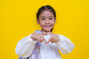 Smiling student showing heart sign with hands on yellow background