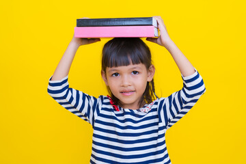 Cute asian girl holding books on head on yellow background
